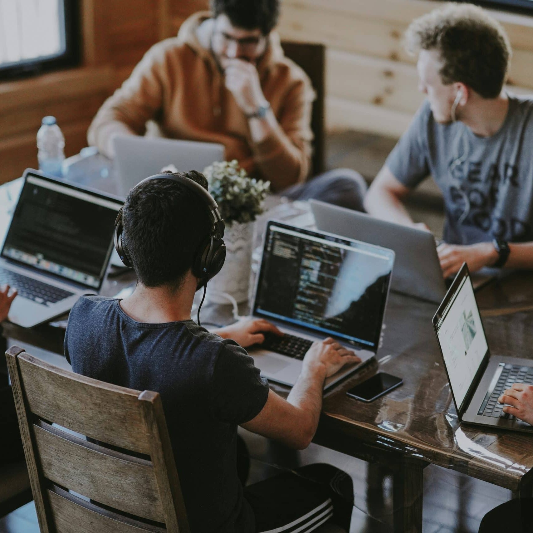headful software Five people using laptops at a wooden table in a casual, collaborative setting, showcasing seamless digital teamwork.