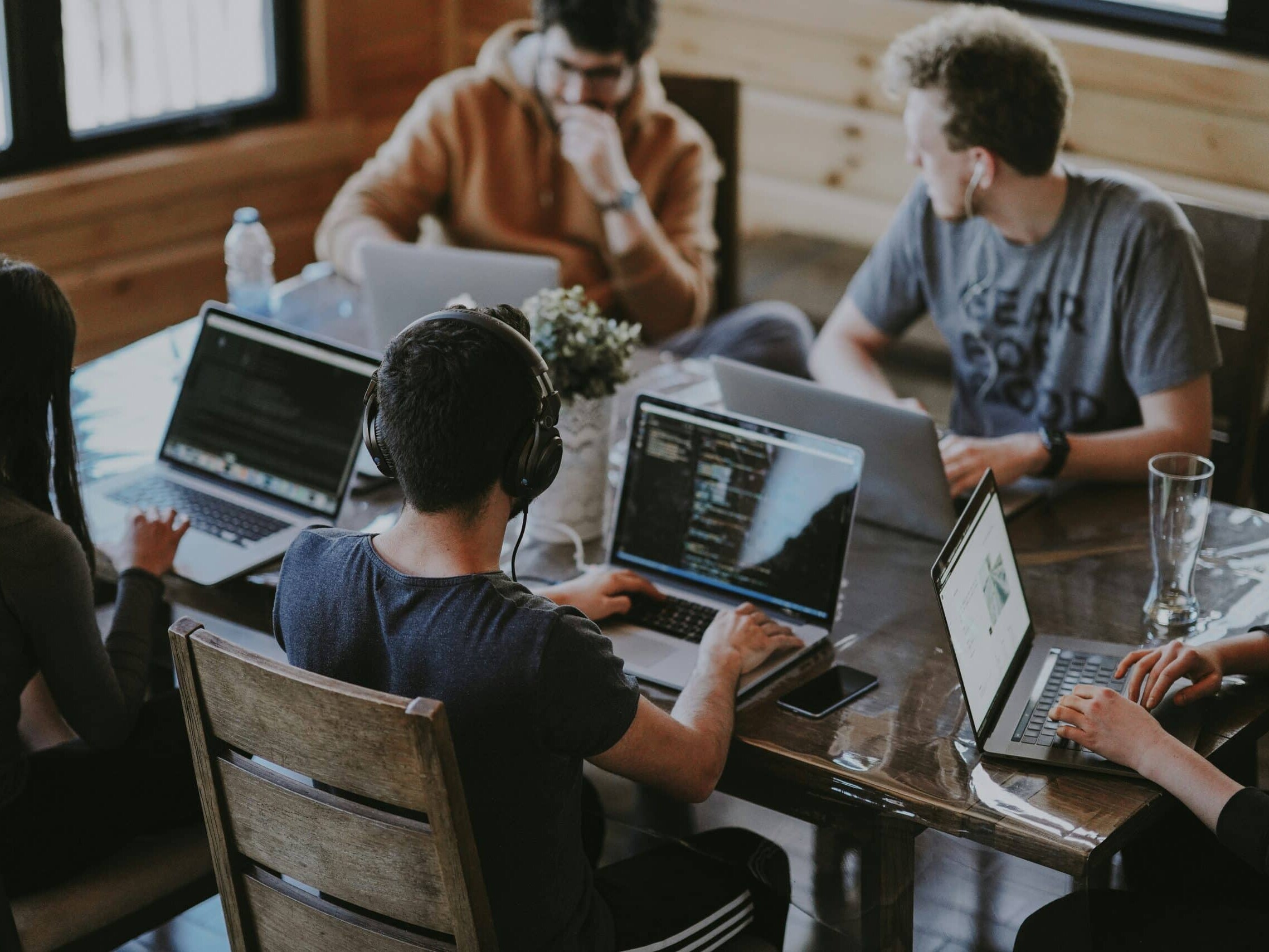 headful software Five people using laptops at a wooden table in a casual, collaborative setting, showcasing seamless digital teamwork.