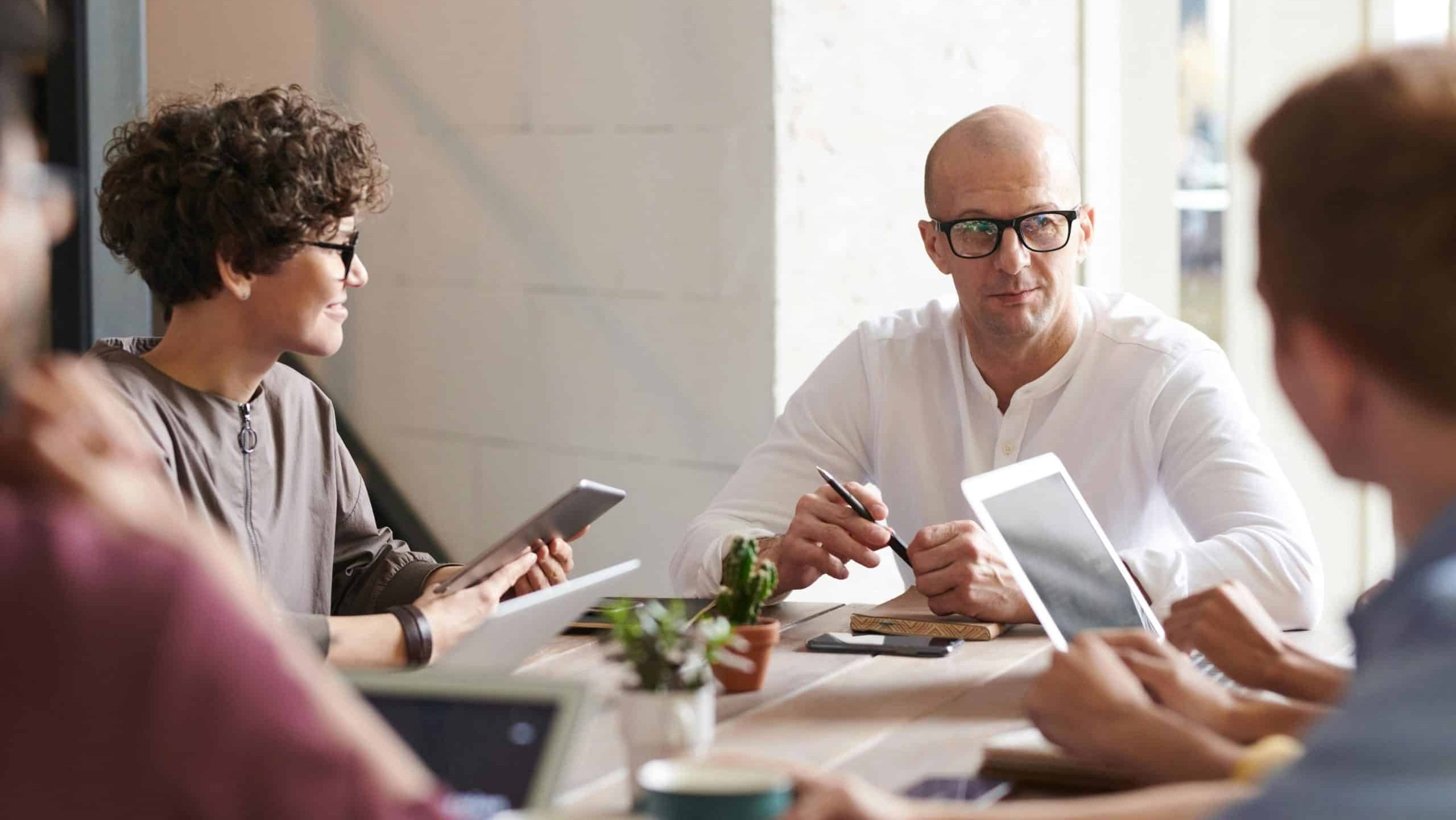 headful software Four people sit around a table in an office meeting, using tablets and notebooks to boost collaboration and productivity as they engage in discussion.